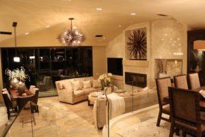 Warmly-lit living room with fireplace, chandelier and dining area